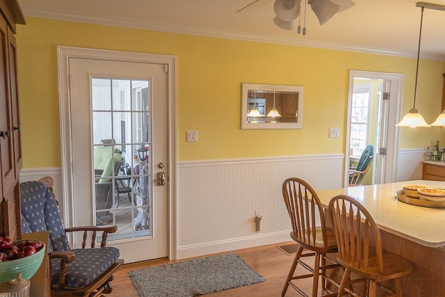 dining space featuring ceiling fan, ornamental molding, wood finished floors, and wainscoting