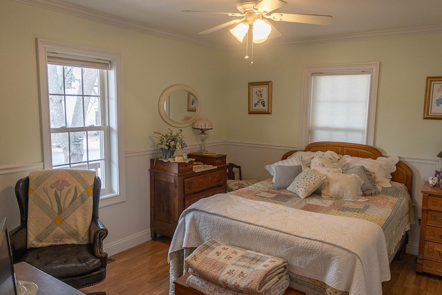 bedroom with ornamental molding, a wainscoted wall, ceiling fan, and wood finished floors