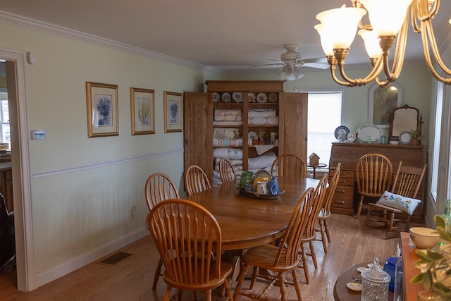 dining space featuring ceiling fan with notable chandelier, wood finished floors, visible vents, baseboards, and ornamental molding