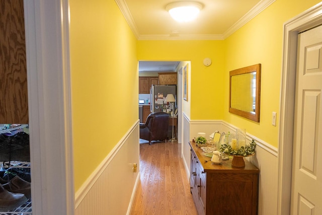 corridor featuring a wainscoted wall, ornamental molding, and light wood-style floors