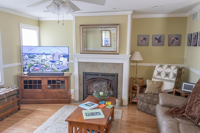 living area with ornamental molding, a tiled fireplace, and wood finished floors