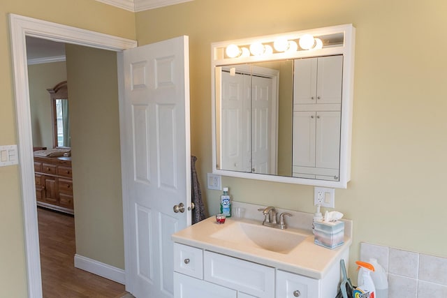 bathroom featuring baseboards, wood finished floors, crown molding, and vanity