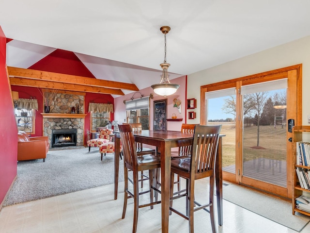 dining space featuring vaulted ceiling, a stone fireplace, light carpet, and a healthy amount of sunlight