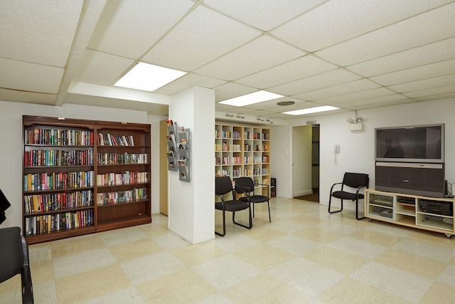 sitting room featuring bookshelves, a drop ceiling, and tile patterned floors