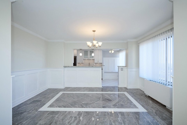 interior space with marble finish floor, a wainscoted wall, crown molding, a decorative wall, and a sink