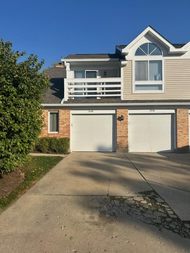 view of front of home featuring driveway, a balcony, a garage, and brick siding