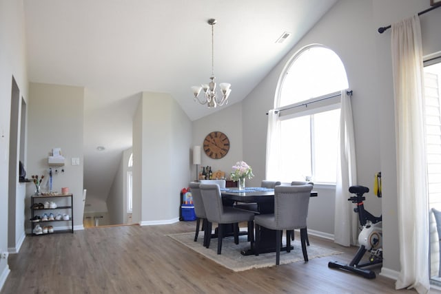 dining space featuring a chandelier, lofted ceiling, wood finished floors, visible vents, and baseboards