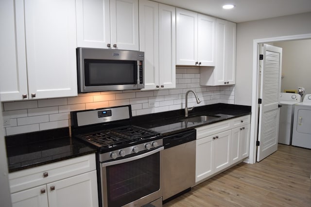 kitchen featuring appliances with stainless steel finishes, washing machine and clothes dryer, a sink, and white cabinets