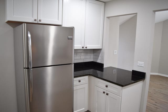 kitchen with white cabinets, decorative backsplash, dark stone countertops, wood finished floors, and freestanding refrigerator