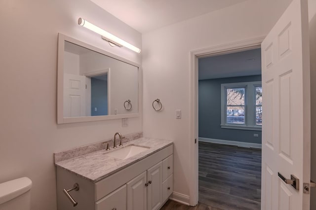 bathroom with wood finished floors, vanity, toilet, and baseboards