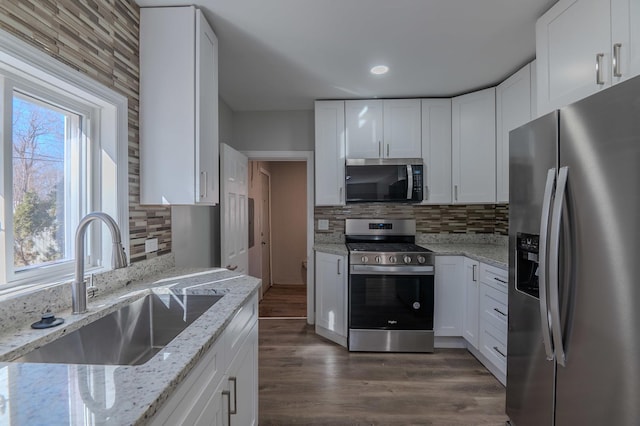 kitchen featuring dark wood-style flooring, decorative backsplash, appliances with stainless steel finishes, white cabinetry, and a sink