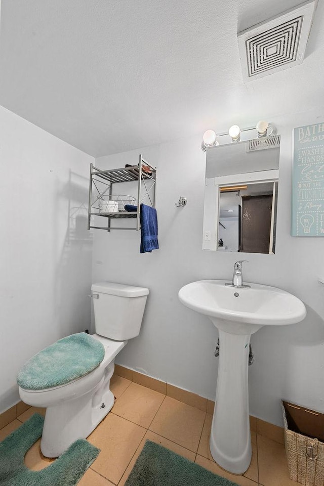 half bathroom featuring toilet, tile patterned flooring, visible vents, and baseboards