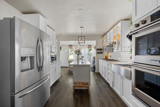 kitchen featuring white cabinets, dark wood finished floors, a kitchen island, stainless steel appliances, and backsplash