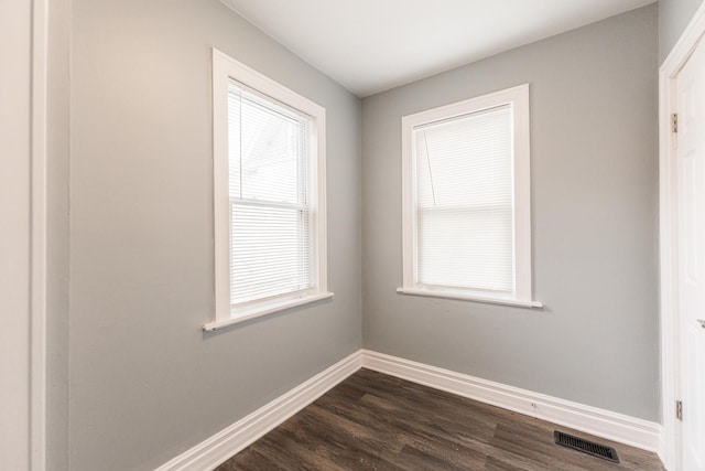 unfurnished room featuring dark wood-style flooring, visible vents, and baseboards