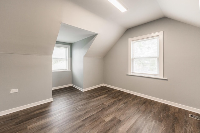 additional living space featuring dark wood-style floors, visible vents, vaulted ceiling, and baseboards