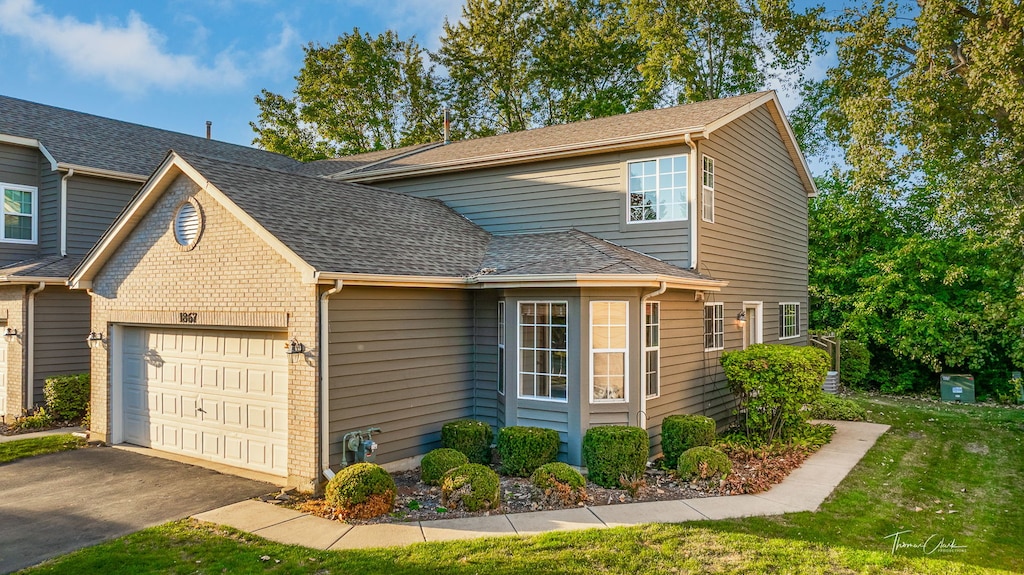 traditional home featuring a garage, roof with shingles, brick siding, and driveway