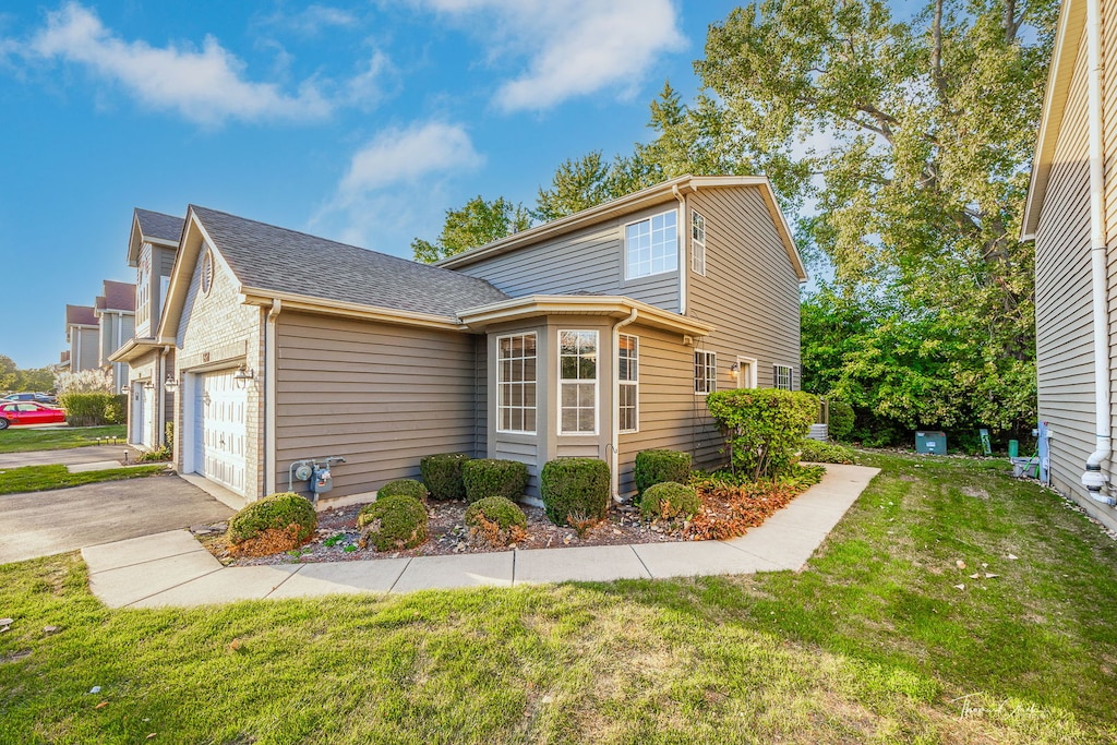 view of side of home with a garage, a yard, aphalt driveway, and a shingled roof