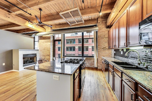 kitchen featuring a tiled fireplace, a kitchen island, light wood-type flooring, black appliances, and a sink