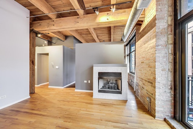 unfurnished living room featuring wooden ceiling, brick wall, wood finished floors, beamed ceiling, and a tiled fireplace