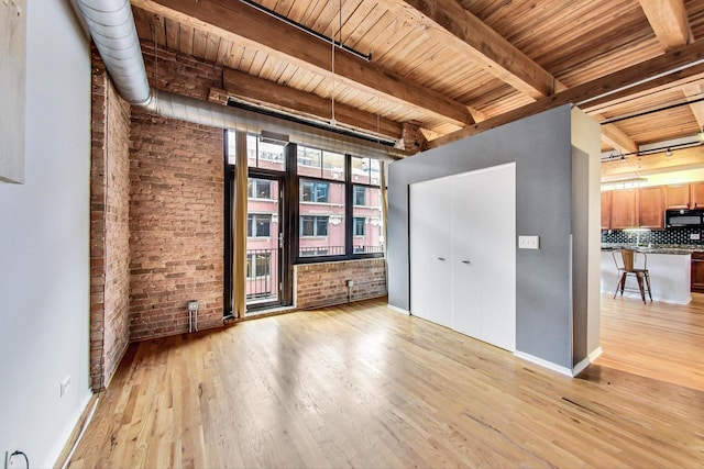 spare room featuring light wood-type flooring, beam ceiling, and brick wall