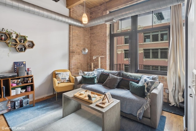 living area featuring a towering ceiling, brick wall, baseboards, and wood finished floors