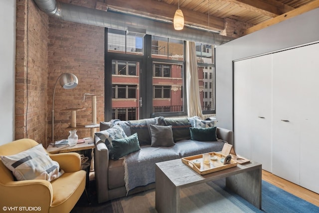 living area featuring brick wall, wood finished floors, and beam ceiling