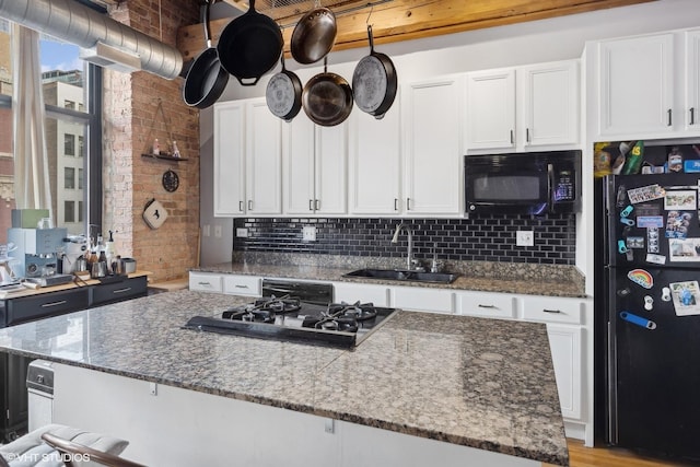 kitchen featuring black appliances, dark stone counters, white cabinets, and a sink