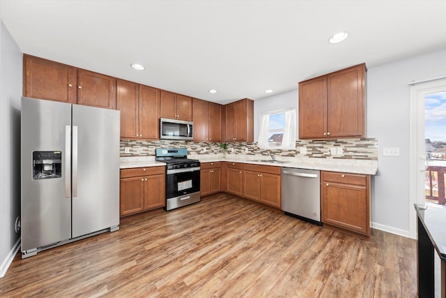 kitchen with light wood-style floors, appliances with stainless steel finishes, light countertops, and backsplash