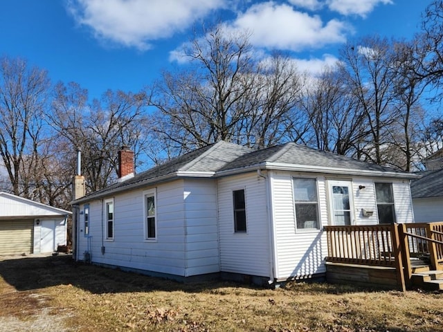 exterior space featuring an outbuilding, a yard, a shingled roof, a chimney, and a deck