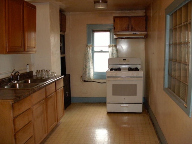 kitchen with dark countertops, baseboards, gas range gas stove, under cabinet range hood, and a sink