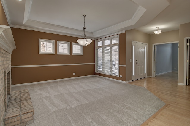 interior space featuring baseboards, light wood-style flooring, a fireplace, ornamental molding, and a raised ceiling