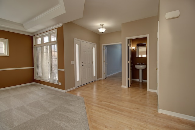 foyer entrance featuring light wood finished floors, baseboards, crown molding, and a tray ceiling