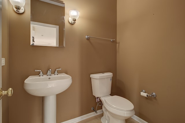 half bathroom with toilet, baseboards, and a sink