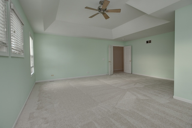 unfurnished room with visible vents, baseboards, light colored carpet, a raised ceiling, and a ceiling fan