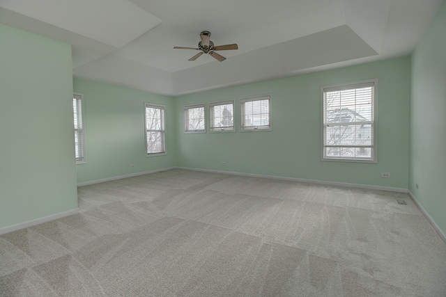 carpeted spare room featuring baseboards, a raised ceiling, and a ceiling fan