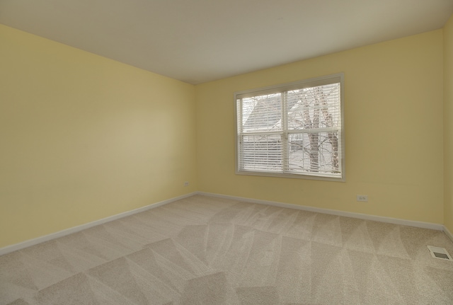 empty room featuring light carpet, visible vents, and baseboards