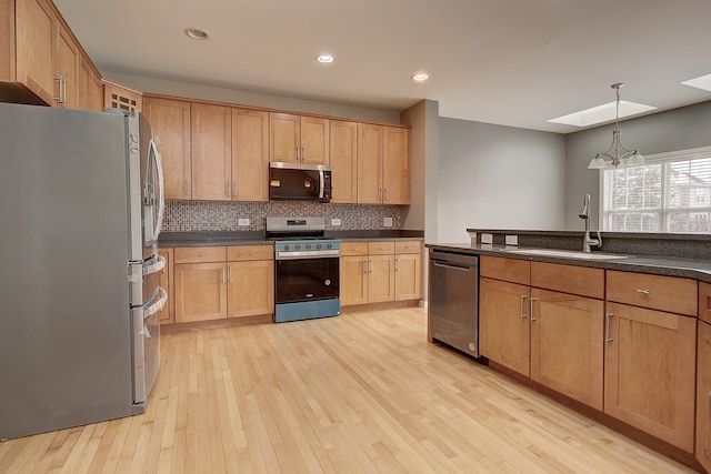 kitchen featuring a sink, stainless steel appliances, dark countertops, and a skylight