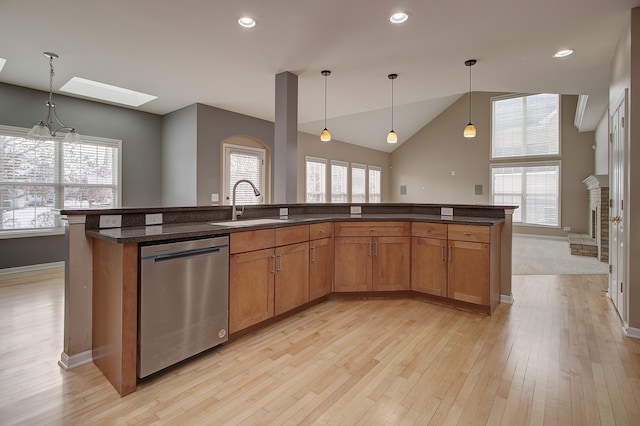 kitchen with vaulted ceiling with skylight, stainless steel dishwasher, light wood-style floors, brown cabinetry, and a sink