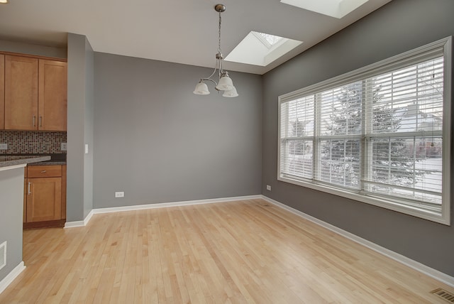 unfurnished dining area featuring a skylight, baseboards, visible vents, and light wood-type flooring