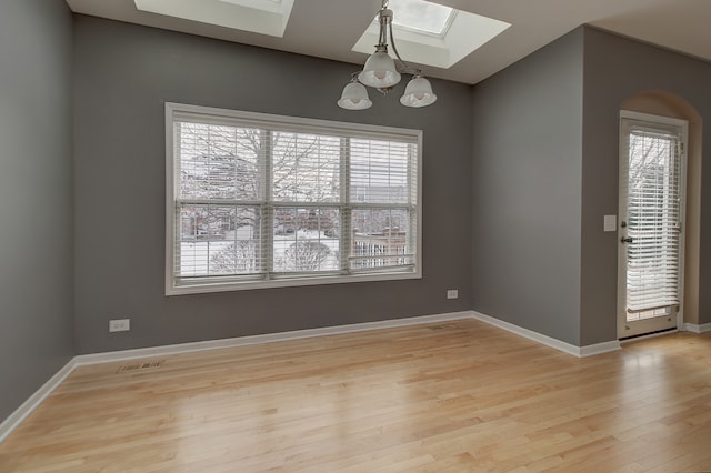 empty room featuring visible vents, a notable chandelier, light wood-style floors, a skylight, and baseboards