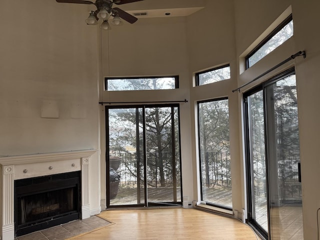 unfurnished living room featuring a fireplace with flush hearth, a high ceiling, visible vents, and wood finished floors