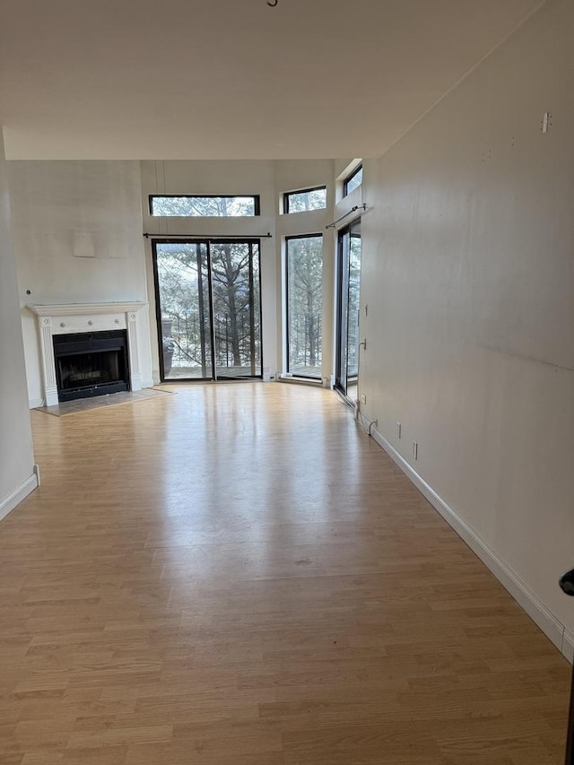 unfurnished living room with light wood-type flooring, a fireplace with flush hearth, a towering ceiling, and baseboards