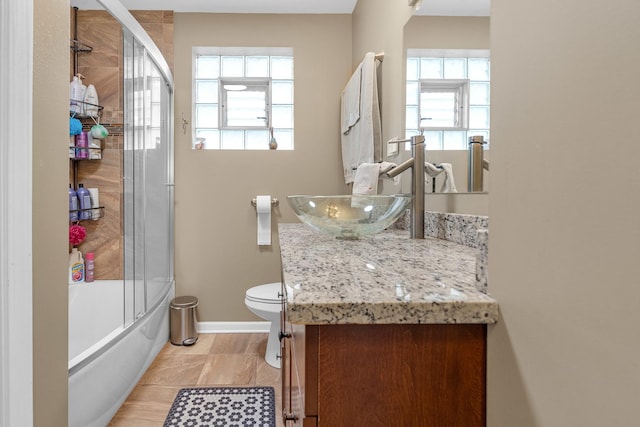 bathroom with toilet, shower / bath combination with glass door, vanity, and baseboards