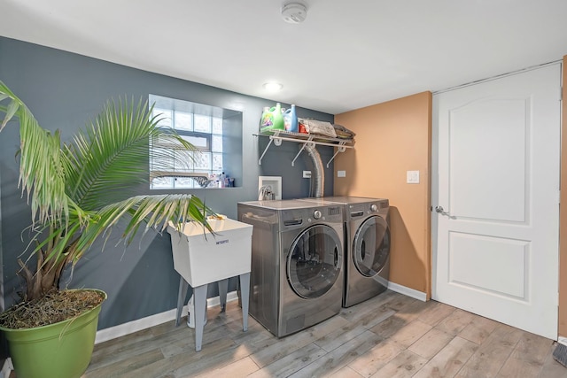 clothes washing area featuring laundry area, light wood-type flooring, washing machine and clothes dryer, and baseboards