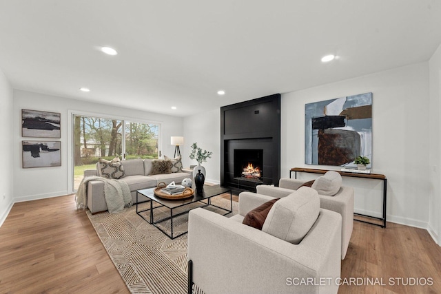 living room featuring a large fireplace, recessed lighting, baseboards, and wood finished floors