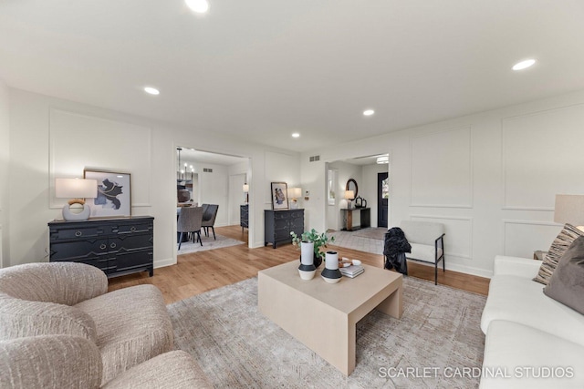 living area featuring light wood finished floors, visible vents, recessed lighting, and a decorative wall