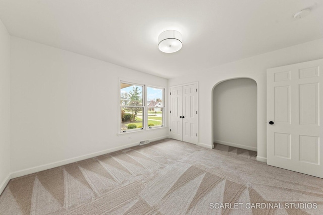unfurnished bedroom featuring baseboards, carpet flooring, and arched walkways