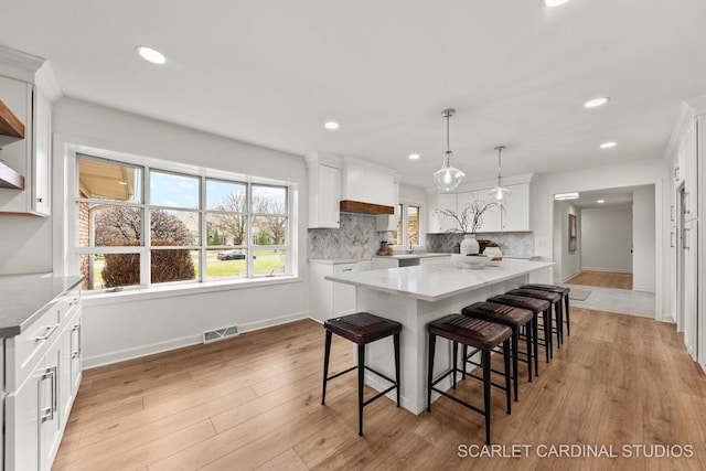 kitchen with white cabinetry, decorative backsplash, a breakfast bar, and visible vents