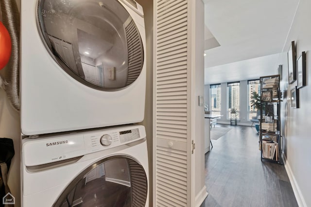 clothes washing area with stacked washer and dryer, baseboards, laundry area, and wood finished floors