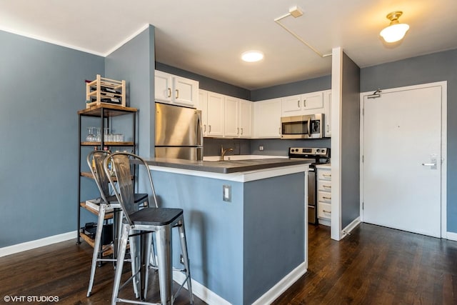 kitchen featuring white cabinets, dark countertops, a breakfast bar area, dark wood-type flooring, and stainless steel appliances